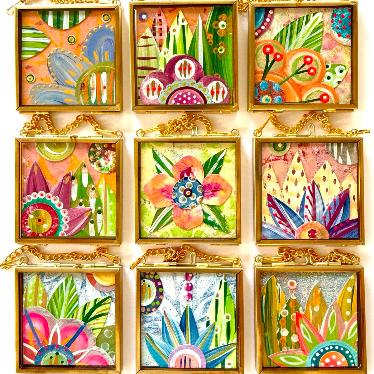 A collection of 2.5" x 2.5" mixed-media collages each is framed between glass in a petite brass hanging frame.
