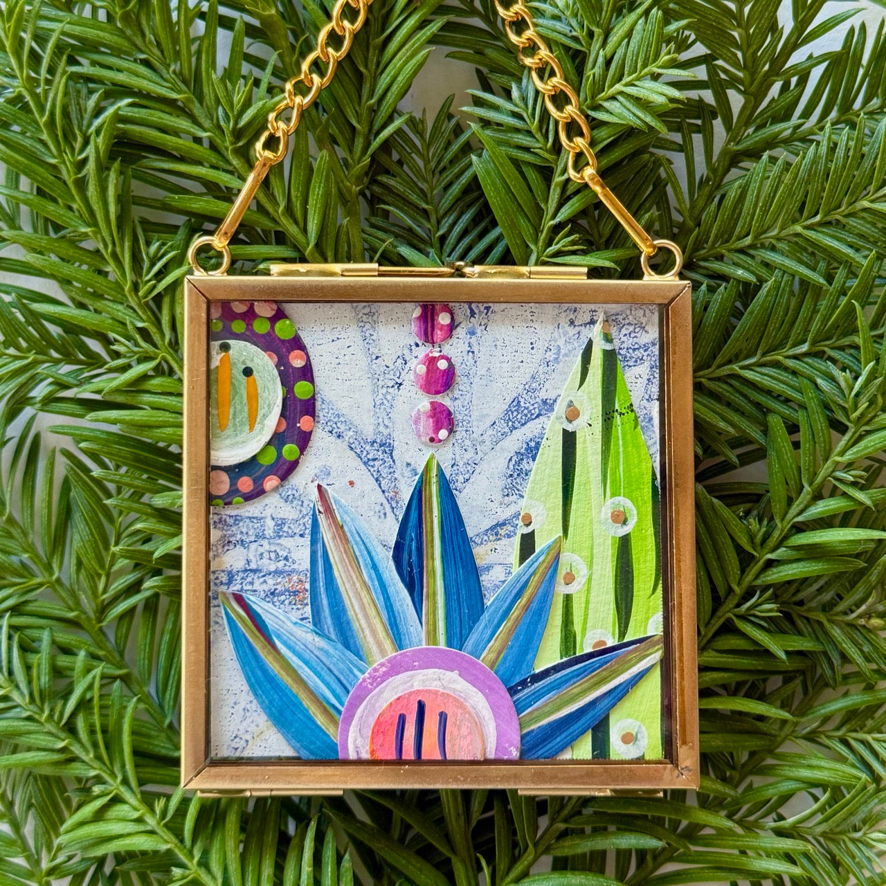 2.5" x 2.5" mixed-media collage is framed between glass in a petite brass hanging frame.