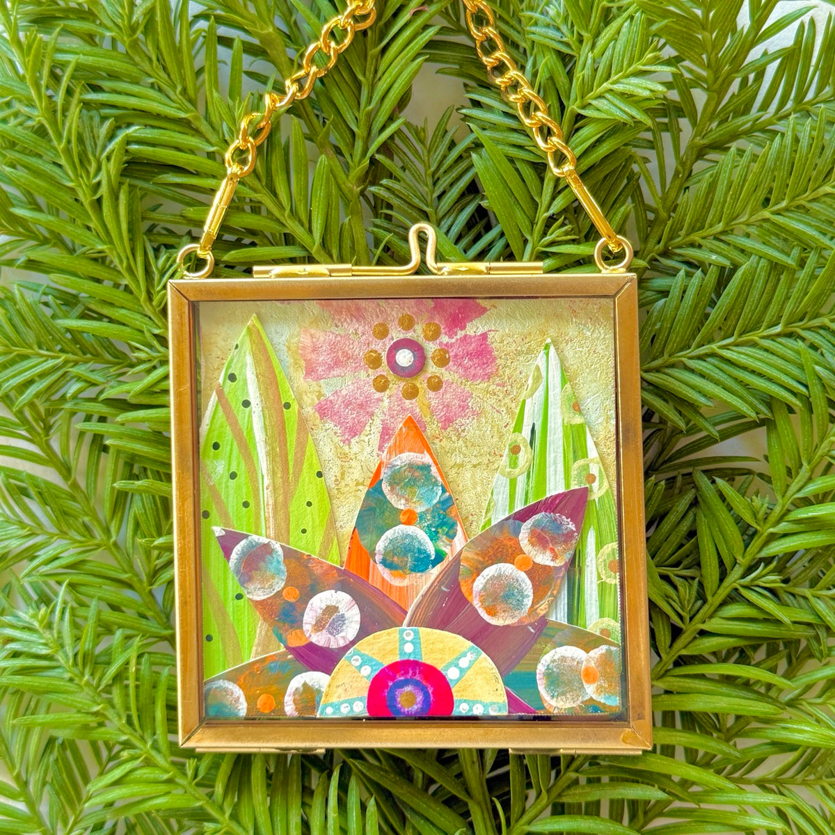 A collection of 2.5" x 2.5" mixed-media collages each is framed between glass in a petite brass hanging frame