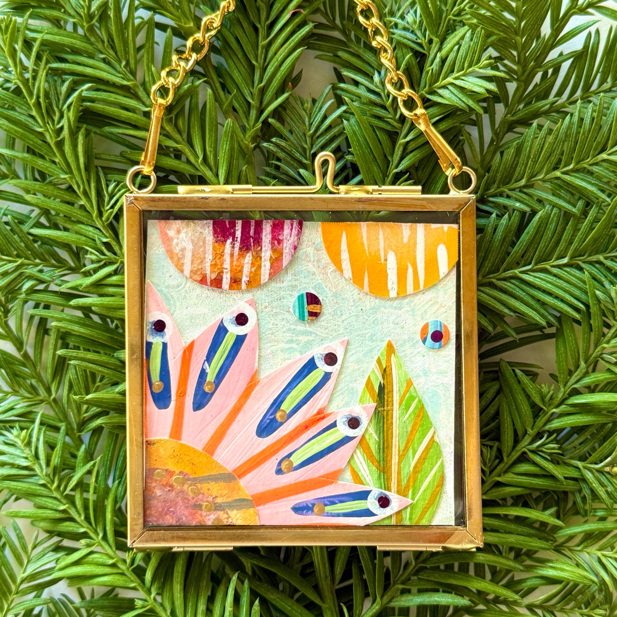 2.5" x 2.5" mixed-media collage is framed between glass in a petite brass hanging frame.